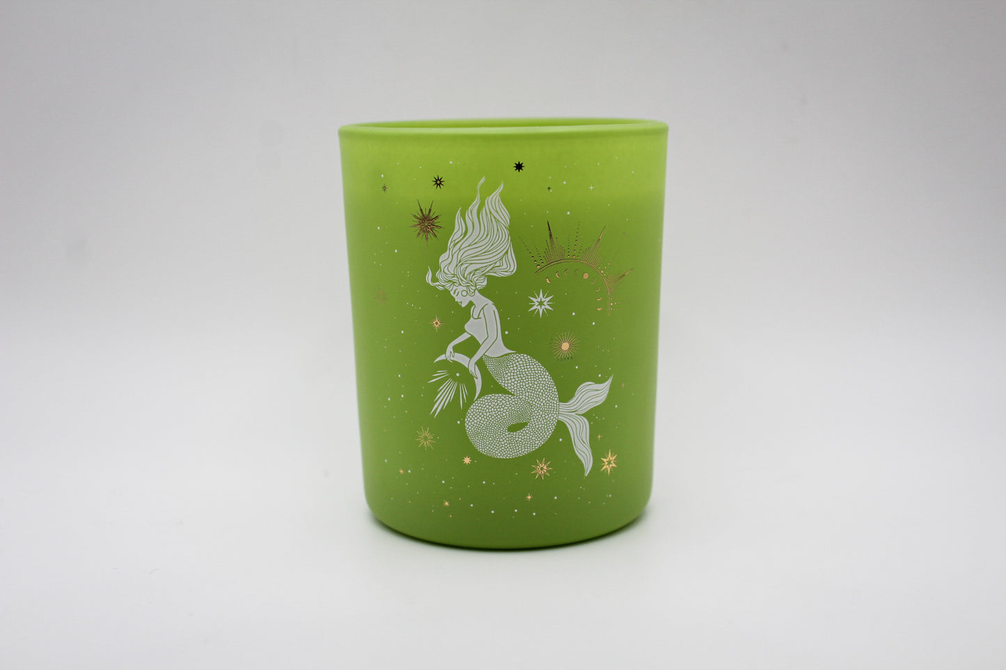 A green candle with decorative patterns including what appears to be a stylized fish and plants, with gold accents.