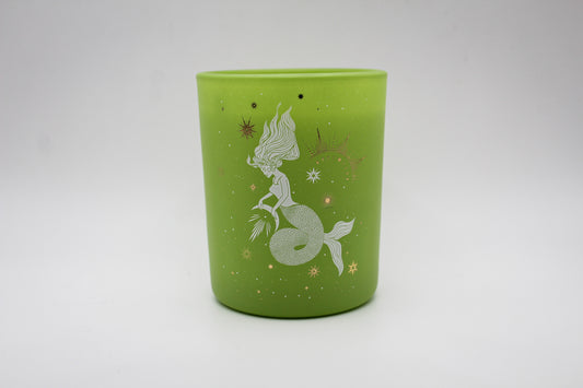 A green candle with decorative patterns including what appears to be a stylized fish and plants, with gold accents.