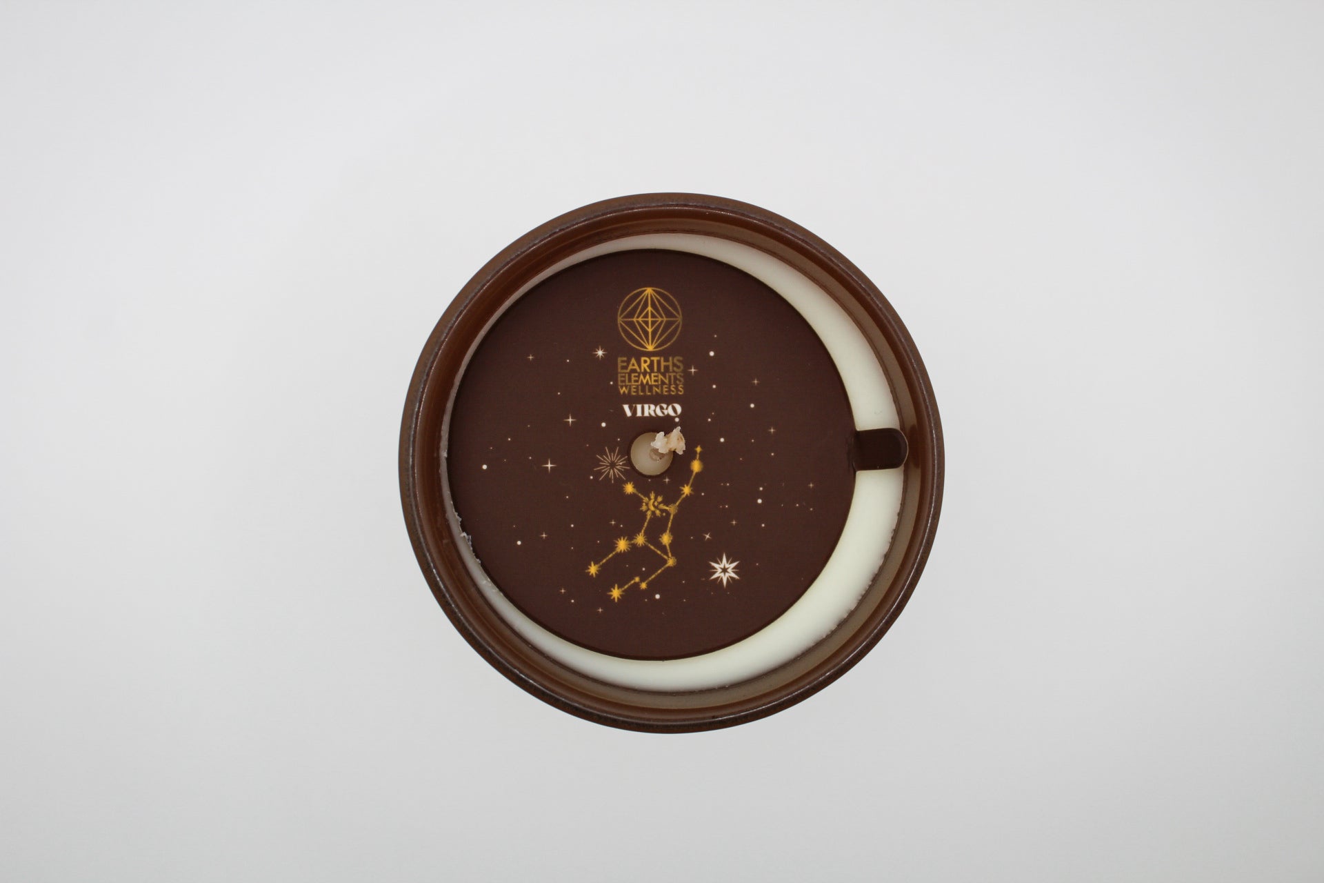 A brown candle with gold and white virgo constellation design.