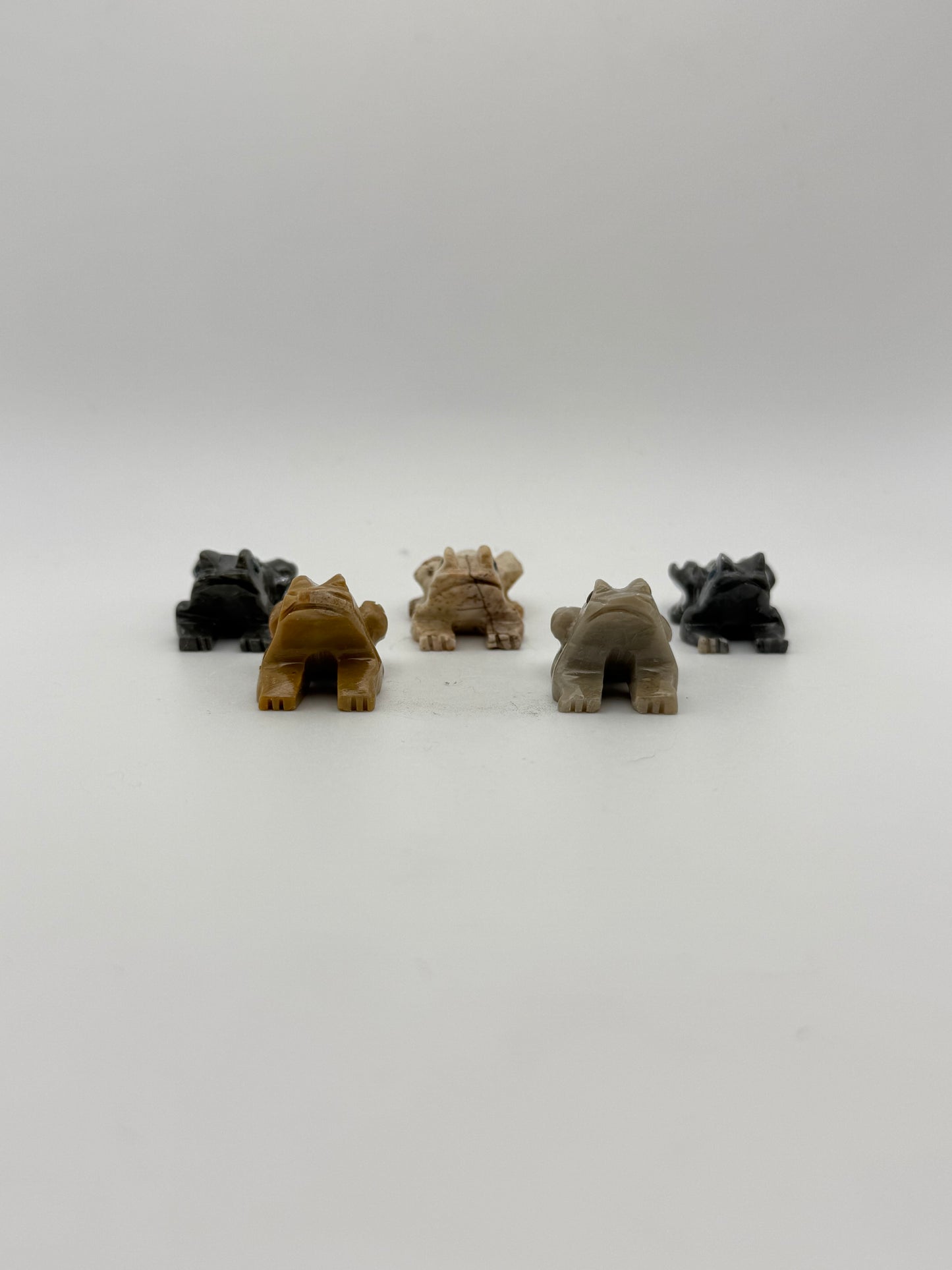 Five small stone sculptures of animals arranged vertically on a white background