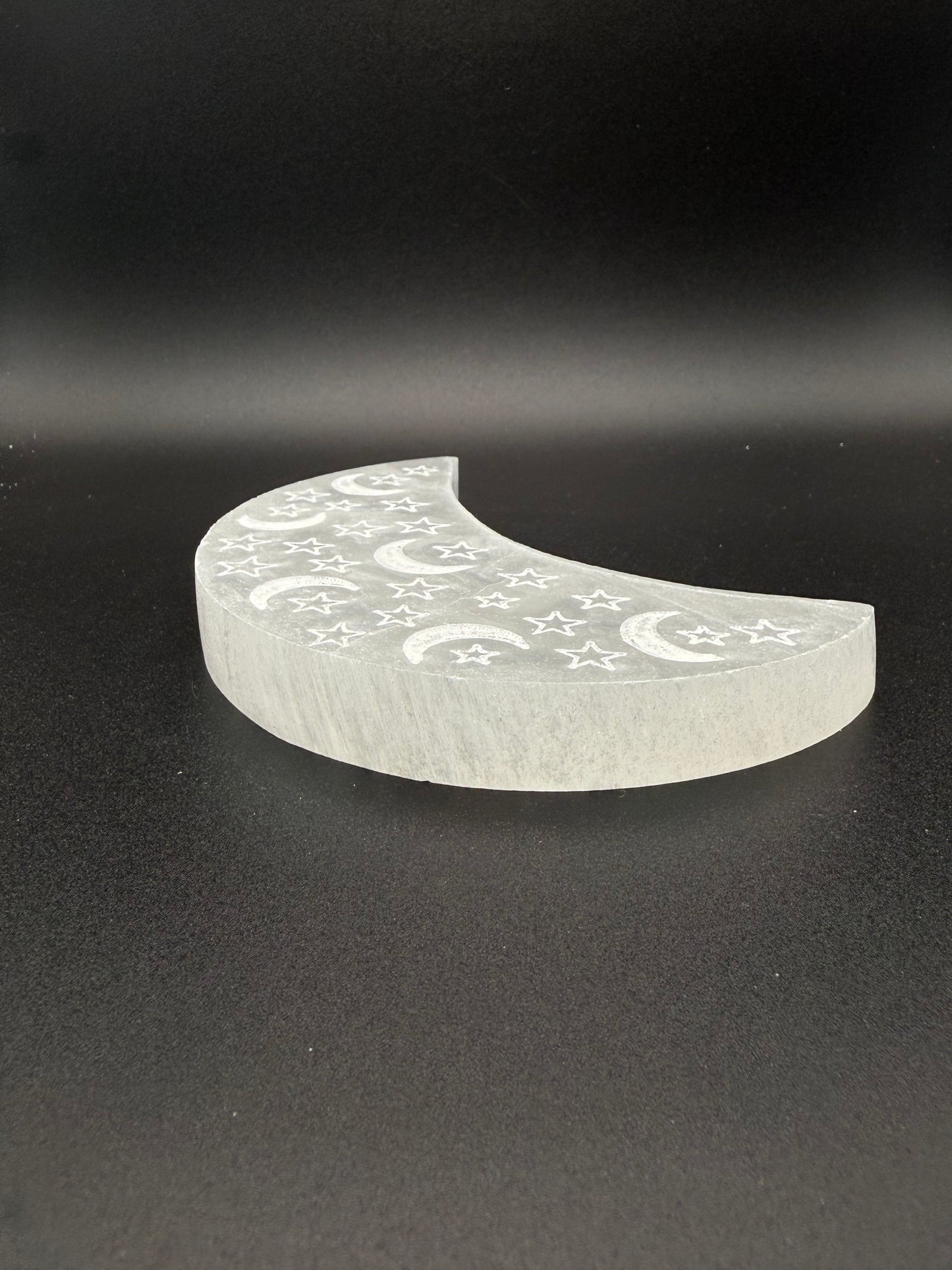 Selenite in the shape of a moon with engraved moons and stars.
