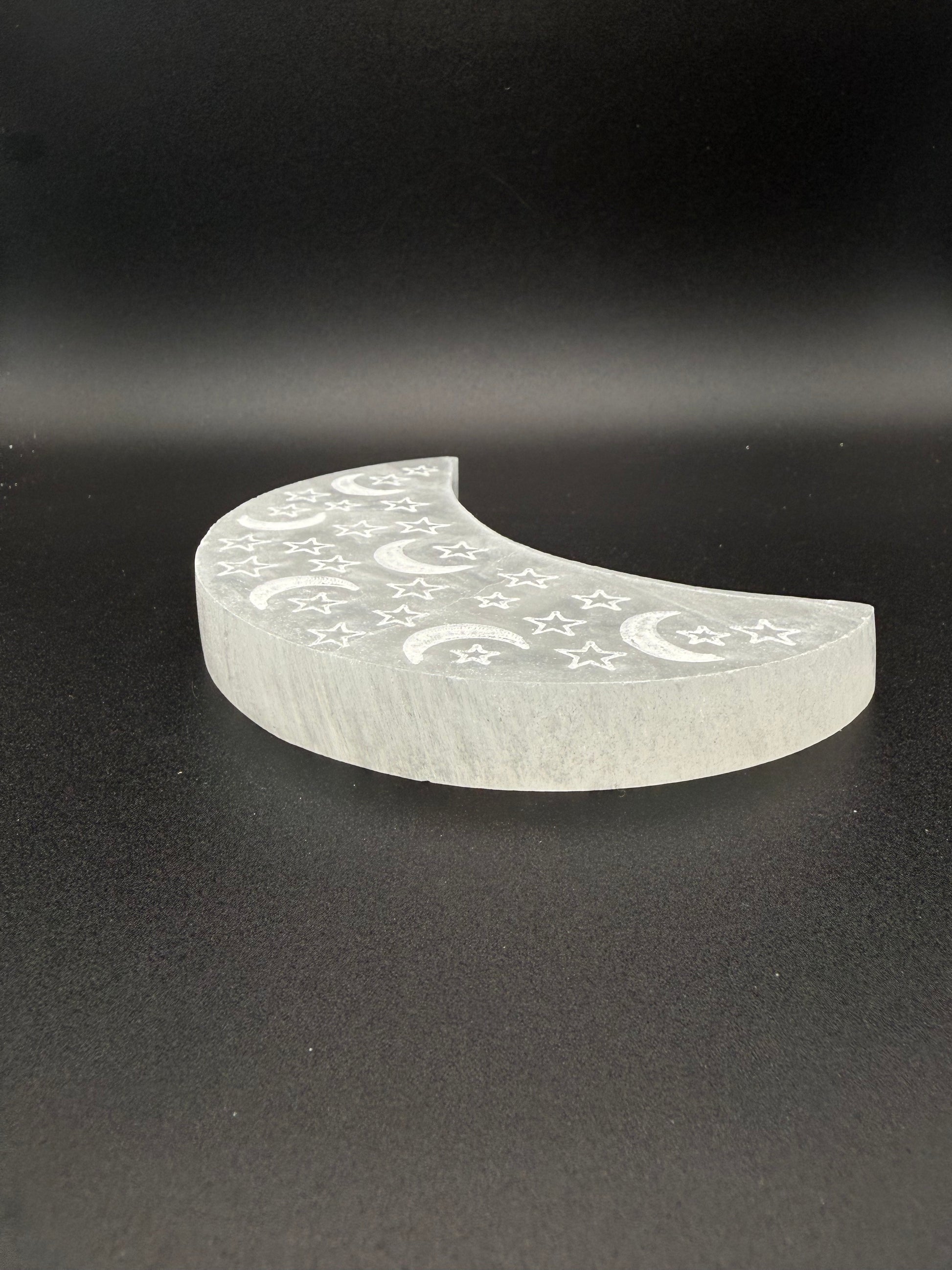 Selenite in the shape of a moon with engraved moons and stars.