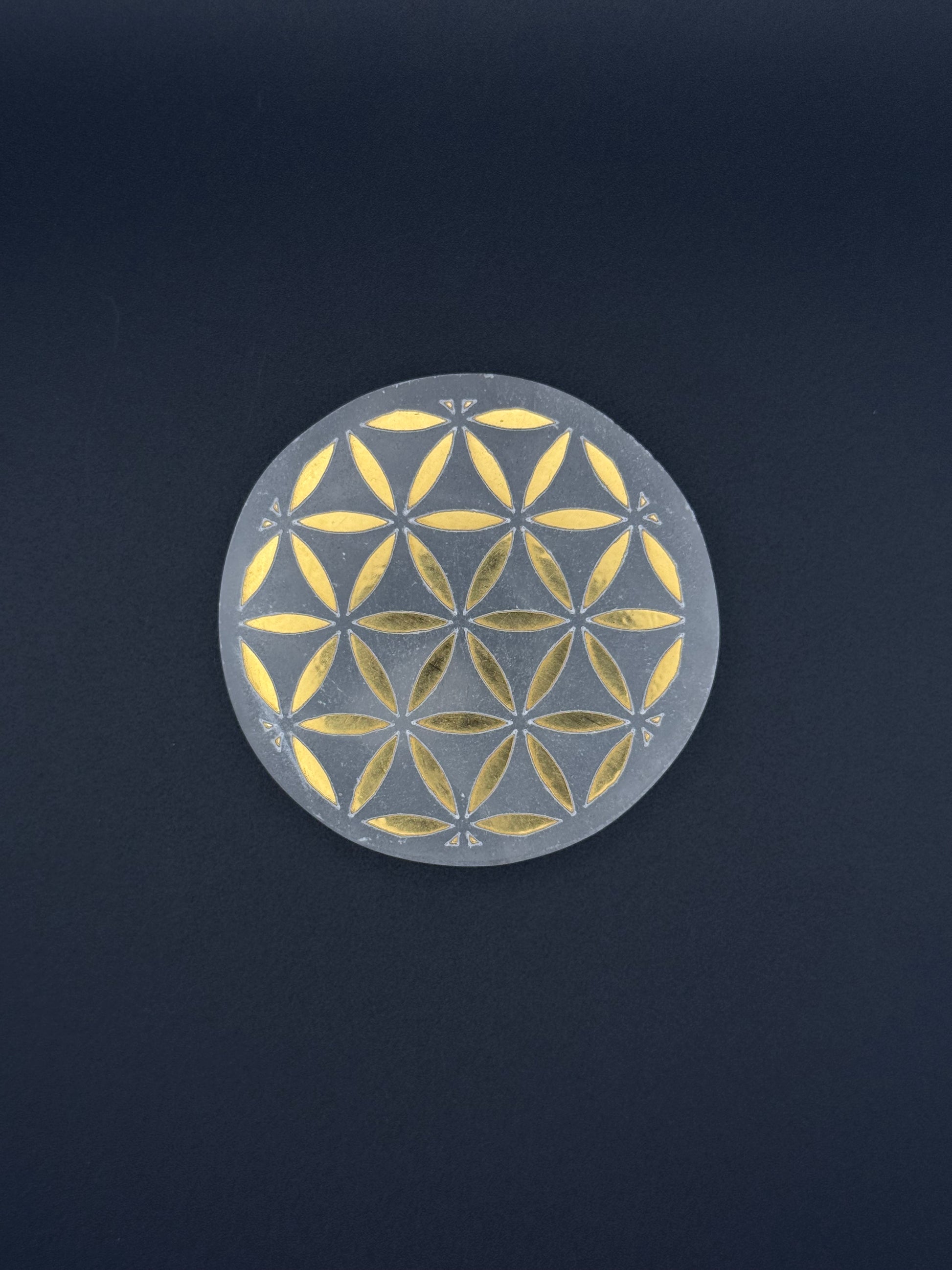 Selenite coaster with engraved flower of life symbol in gold.