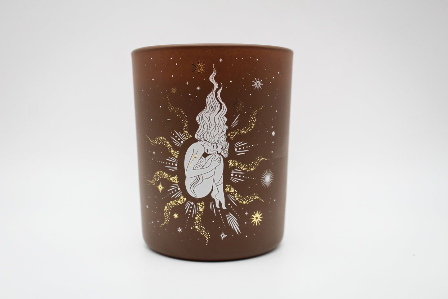 A brown candle with gold and white virgo constellation design.
