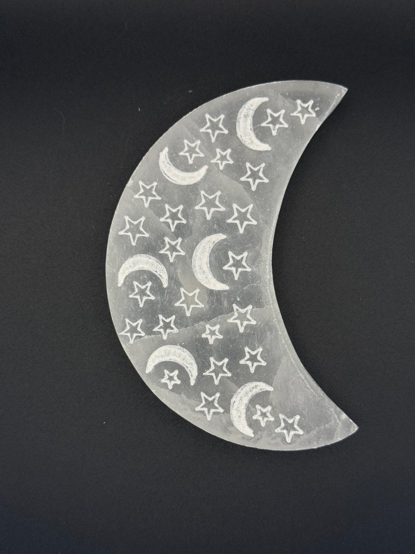 Selenite in the shape of a moon with engraved moons and stars.