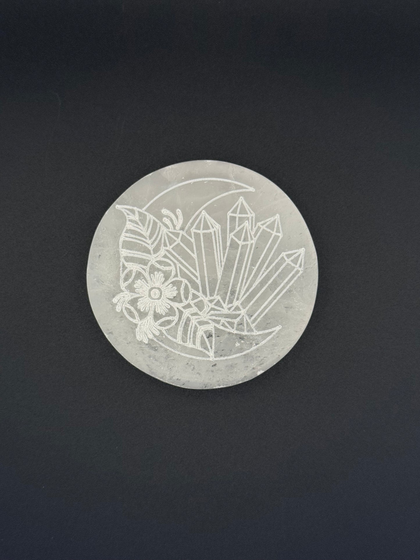 Selenite coaster with an engraved image of crystals and a moon.