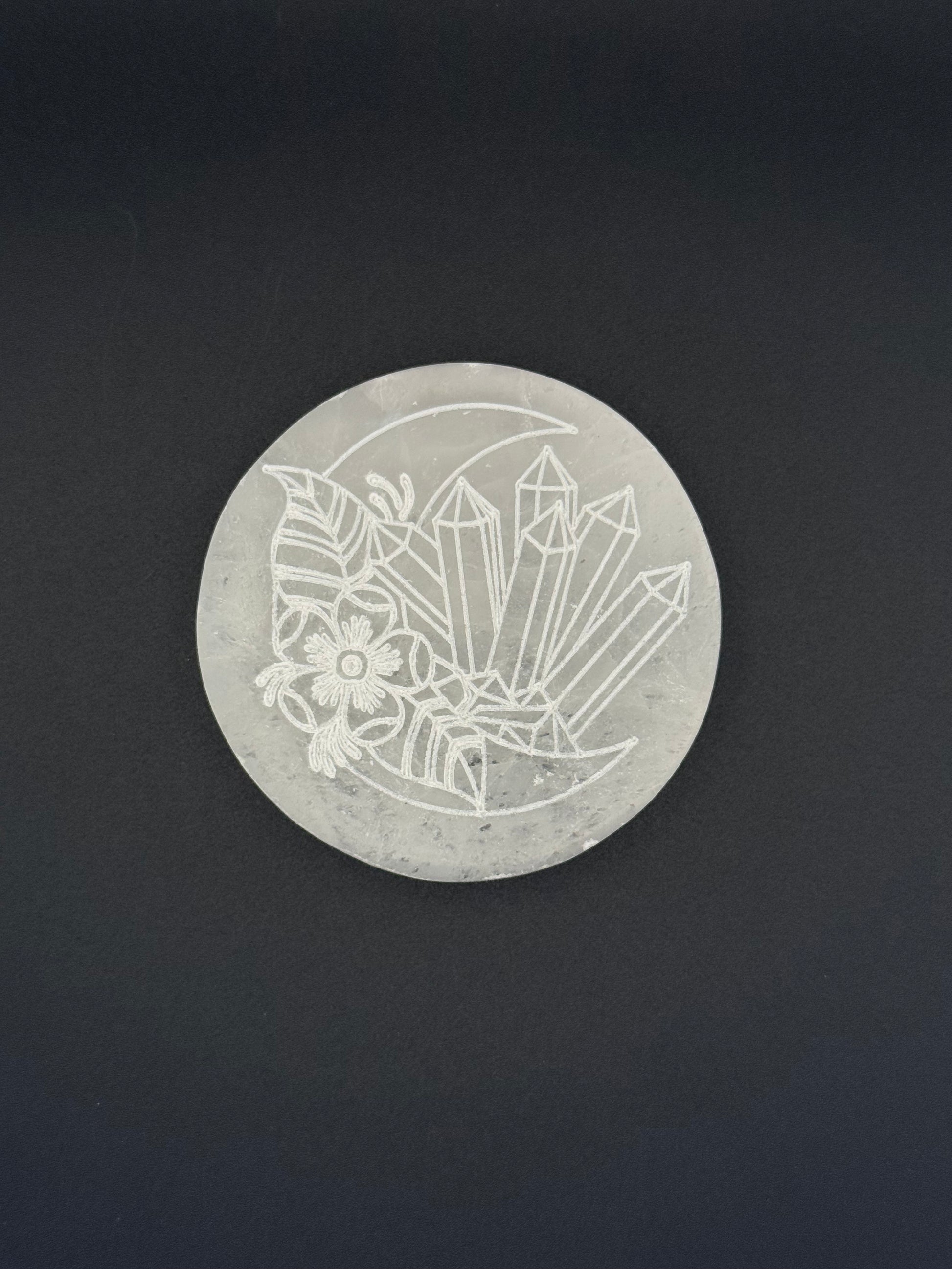 Selenite coaster with an engraved image of crystals and a moon.