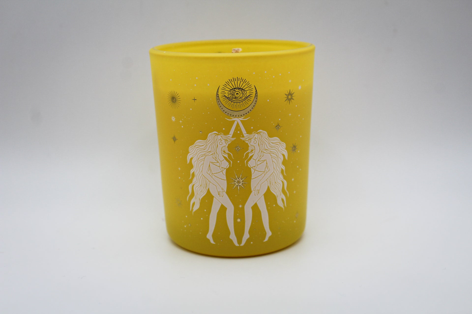 A yellow candle with white and silver geometric patterns and designs representing the constellation Gemini.
