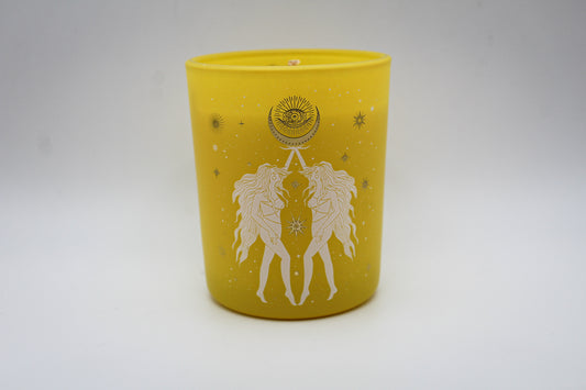 A yellow candle with white and silver geometric patterns and designs representing the constellation Gemini.